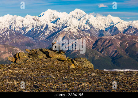 Un randonneur reposant sur des rochers observe McGinnis Peak, Mount Moffit et Mount Hayes qui s'élèvent au loin; Alaska, États-Unis d'Amérique Banque D'Images