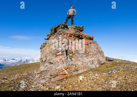 Un randonneur pose au sommet d'un rocher sur une crête de la chaîne de l'Alaska; Alaska, États-Unis d'Amérique Banque D'Images