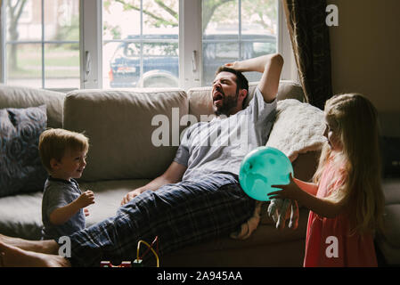Un vieux père est couché sur le canapé tandis que ses enfants jouer autour de lui. Banque D'Images