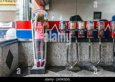 Une jeune fille se tient sur une échelle à un lavage de voiture à côté de gumball machines. Banque D'Images