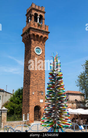 Murano, Italie - 19 juillet 2019 : un arbre fabriqué à partir de verre de Murano avec le clocher médiéval de l'église San Stefano dans le bcakground, sur l'est de Venise Banque D'Images