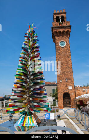 Murano, Italie - 19 juillet 2019 : un arbre fabriqué à partir de verre de Murano avec le clocher médiéval de l'église San Stefano dans le bcakground, sur l'est de Venise Banque D'Images