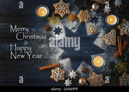Biscuits au gingembre, épices et brûler des bougies sur une étoile de sucre glace sur un fond de bois bleu foncé, texte Joyeux Noël et Bonne Année, Banque D'Images