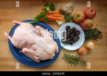 De canard cru prêt à cuire et d'ingrédients tels que les pommes, prunes cuites, légumes et fines herbes sur un comptoir de cuisine en bois, high angle view from above Banque D'Images