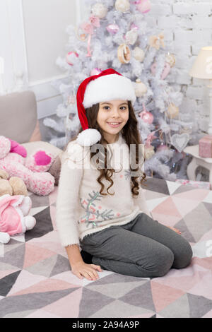 Bonne année. Demandez si la personne a une liste de souhaits. Petit enfant porter santa hat fêter le nouvel an à la maison décoration intérieure. Matin avant Noël. Maison de vacances de nouvel an. Enfant fille dans la chambre avec des jouets. Banque D'Images