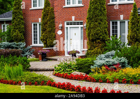 Majestueuse maison en brique avec un chemin sinueux et un aménagement paysager avec plantes et fleurs dans la cour avant; Hudson, Québec, Canada Banque D'Images