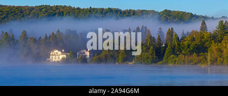 La brume se pose au-dessus du lac a la Truite à l'aube avec des nuages bas qui pendent sur la forêt le long du rivage; Québec, Canada Banque D'Images