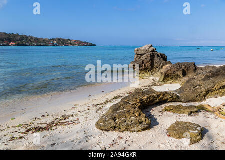 Les roches altérées sur plage de sable blanc, de Nusa Lembongan, à Bali, Indonésie. Océan bleu clair avec des bateaux au-delà. Nusa Penida au loin. Banque D'Images