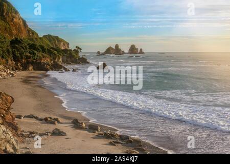 La mer de Tasman et une belle plage isolée avec des formations rocheuses spectaculaires, sur la côte ouest de l'île du sud de la Nouvelle-Zélande, au coucher du soleil. Banque D'Images