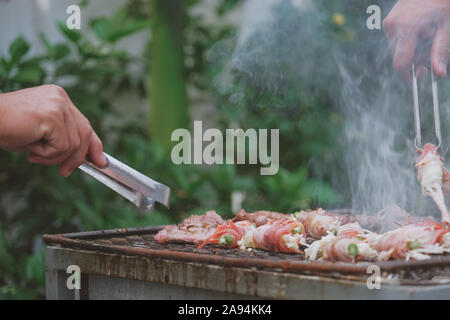 La bacon enveloppé de champignons de l'aiguille d'être rôti au fusain sur le grill. Champignons grillés sur le Barbecue grill en acier sur un charbon cuisinière brûlé Banque D'Images