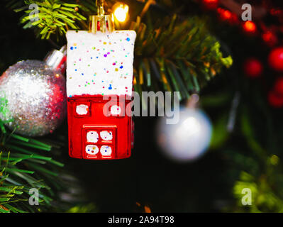 Un jouet à la forme d'une maison rouge se bloque sur un arbre de Noël. Décoration d'arbre de Noël sous la forme d'un hiver maison accrochée à un arbre de Noël. À Banque D'Images