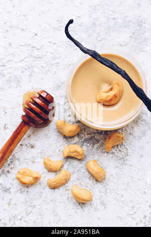 Beurre de noix de cajou dans le verre. Des matières organiques de cajou pâte sur fond gris, avec du miel et de la vanille. Aliments naturels sains concept. Vue d'en haut. Banque D'Images