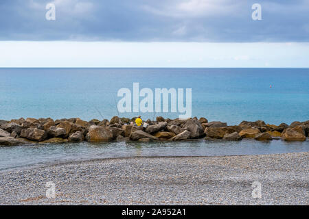 Un homme non identifiables avec des seaux et barres de pêches sur les rochers le long de la côte de Vintimille, Italie, sur la Riviera italienne. Banque D'Images