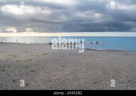 Un homme seul non identifiables, les promenades le long de la côte de Vintimille, Italie sous un ciel couvert matin comme les rayons de soleil à travers les nuages de pointe Banque D'Images