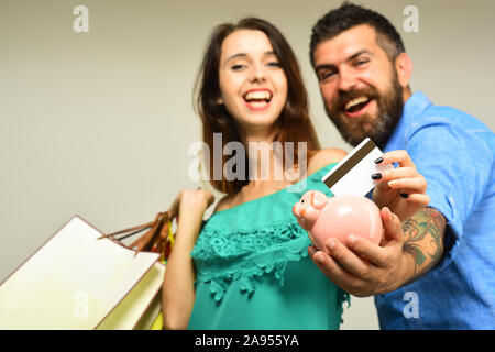 Guy avec barbe et dame avec des visages souriants faire du shopping. Couple in love est titulaire de la carte de crédit sur le fond gris. Les dépenses d'achats et de concept. Homme à barbe est titulaire d'une carte de crédit et tirelire, Close up. Banque D'Images