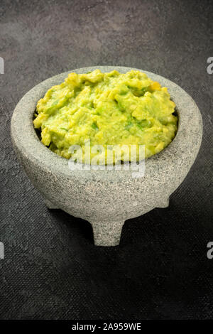 Le guacamole dans un molcajete, avocat mexicain sauce trempette dans le mortier traditionnel en pierre, sur un fond noir avec une place pour le texte Banque D'Images