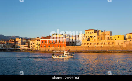 Chania, Crète, Grèce. Vue sur le port vénitien au lever du soleil, bateau de pêche se dirigeant vers la mer. Banque D'Images