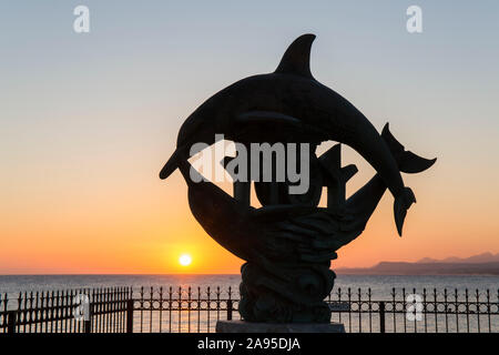 Rethymno, Crète, Grèce. Silhouette de l'emblématique statue de dauphin au lever du soleil. Banque D'Images