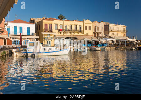 Rethymno, Crète, Grèce. Vue sur le port vénitien, tôt le matin, les bâtiments en bord de mer se reflètent dans les eaux ondulées. Banque D'Images