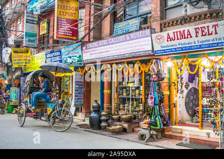 Un extracteur de pousse-pousse en attente de client dans l'avant du magasin qui vend des bols tibétains dans la région touristique de Thamel à Katmandou. Banque D'Images