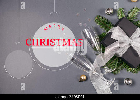 Bonne Année, Noël bauble avec cadeaux faits main noire décorée de ruban d'argent, les branches d'arbres, deux verres de champagne confetti sur grey background Banque D'Images