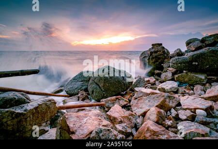 L'eau de l'océan des vagues sur la plage de rock avec beau coucher de soleil Ciel et nuages. Éclaboussures des vagues de la mer sur la pierre en mer sur la côte de l'été. Nature Paysage. Scieries Banque D'Images