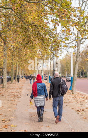 Vue arrière de couple marchant sur le trottoir, le long du Mall dans le centre de Londres, Royaume-Uni, en automne, tenant des peaux de banane à la recherche de poubelle de déchets de litière. Banque D'Images