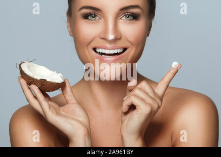 Belle jeune femme avec une noix de coco et la crème hydratante isolé sur fond gris Banque D'Images