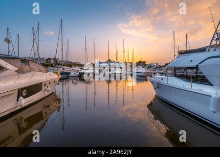 Port de Cala d'Or au coucher du soleil. Bateaux en premier plan avec des restaurants et des palmiers dans la distance, ciel coloré avec la réflexion. Mallorca, Espagne. Banque D'Images