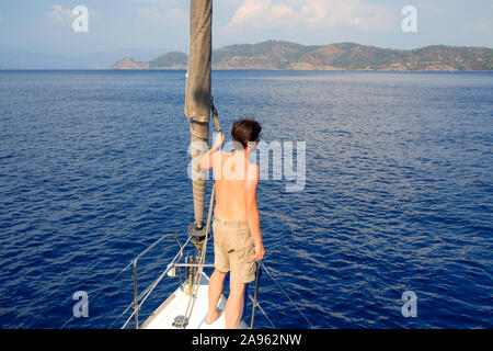 L'homme en short se dresse sur la plate-forme près de la voile, de la voile et le yachting, concept. Guy sur un yacht voyage sur le fond de la mer. Banque D'Images