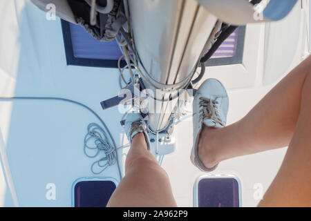 Skipper d'un voilier. Monter le mât, la conduite d'un yacht, le yachting. Les pieds des femmes en blanc sneakers sur les étapes. vue depuis le mât. Banque D'Images