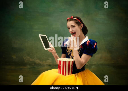 Jeune danseuse de ballet comme un Blanc Neige avec tablet à cinéma avec pop-corn. Ballerine souple comme caractère de fairytail dans des vêtements. Histoire Moderne de contes classiques. Les émotions, la comparaison des époques. Banque D'Images