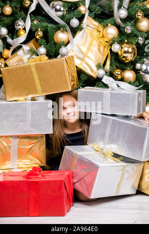 Portrait de preteen girl wearing blue dress assis parmi gifts près de l'arbre de Noël décoré heureux d'obtenir de nombreux cadeaux le lendemain Banque D'Images