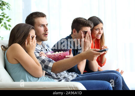 Peur groupe des amis à regarder un film d'horreur à la tv assis sur un canapé dans la salle de séjour à la maison Banque D'Images
