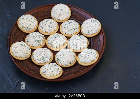 Snack sur des craquelins avec du fromage est situé sur une plaque sur un fond sombre, vue du dessus Banque D'Images