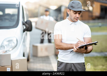 Portrait d'homme en uniforme de livraison l'article avec les documents près de la fourgonnette véhicule, collègue de déchargements des parcelles sur l'arrière-plan Banque D'Images