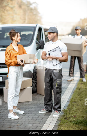 Liste de messagerie avec la livraison des marchandises sur une jeune femme par cargo van véhicule, auteur avec un carton des parcelles sur l'arrière-plan Banque D'Images