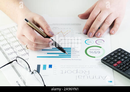 Gros plan du business woman's hands holding pen et en montrant les tableaux financiers. Mains visibles, un stylo, lunettes et calculatrice sur blanc 24. Banque D'Images