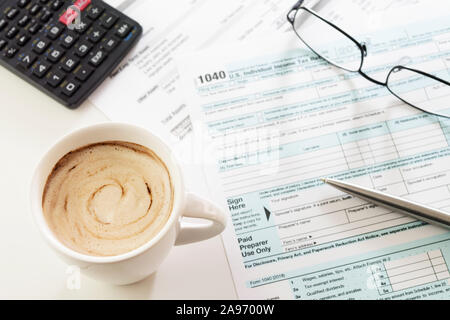 Tasse de café crémeux sur tableau blanc avec déclaration des États-Unis le formulaire 1040, stylo, calculatrice et visibles des lunettes. La fiscalité, la comptabilité, les affaires, les finances Banque D'Images