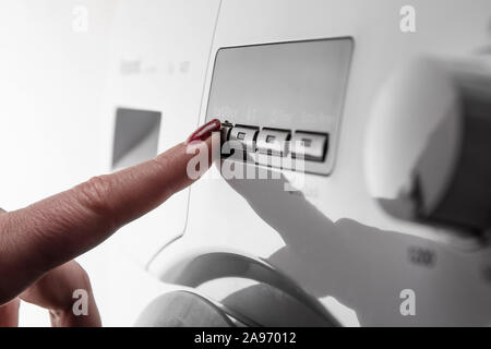 Closeup détail de l'index de la femme avec du vernis à ongle poussant le bouton de démarrage sur machine à laver moderne blanc Banque D'Images