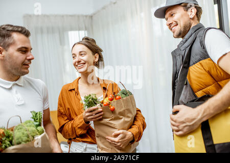 Cheerful courier dans la prestation uniforme des produits alimentaires frais d'une jeune famille à la maison. Magasinage en ligne et de livraison à domicile concept Banque D'Images