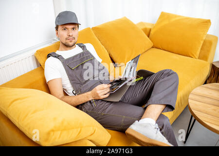 Handyman in workwear assis sur le divan jaune tout en se reposant après le travail Banque D'Images