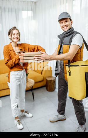 Portrait of a handsome courier en uniforme la livraison pizza avec sac thermique à un client à la maison, heureux femme qui reçoit sa commande Banque D'Images