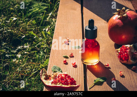 La lumière du soleil à l'huile de graines de grenade, de sérum dans le flacon en verre sur fond de bois. Concept de vie de l'anti-âge. Banque D'Images