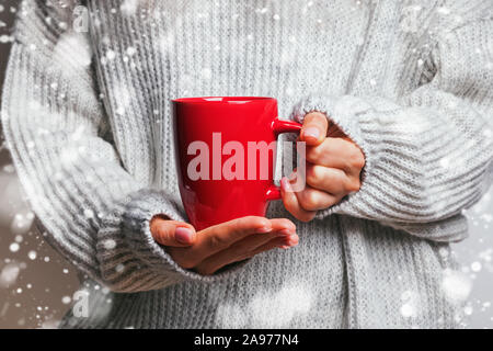 Dans les mains des femmes chandail tricoté holding mug rouge avec thé, café ou cacao close-up. Banque D'Images