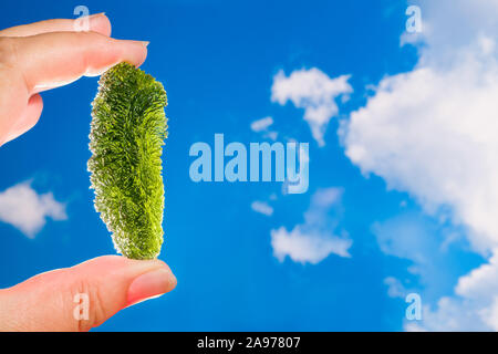 Pierre semi précieuse moldavite rare sur fond de ciel bleu. Sunlit gem météorique. Rock tektite moussus de l'apparence et la surface rugueuse au collector's main. Banque D'Images