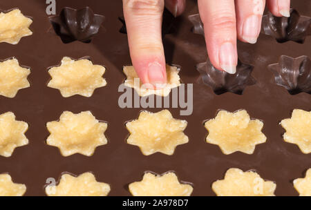 Les doigts femelle brown de remplissage du moule en silicone. Cuisson des noix de coco Noël cupcakes. Plein de fleurs ornés sweet pâte crue. Maison de cookies en forme plastique. Banque D'Images