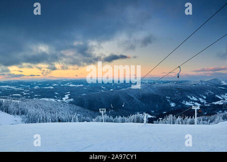 Soir paysage d'hiver dans les montagnes et forêts de sapins sur le coucher du soleil. Collines couvertes de neige après de fortes chutes de neige. Pistes de ski de l'arrière-pays de neige Banque D'Images