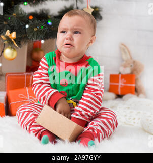 Mauvais Noël. Petit bébé elfe à présent fort de pleurer près de l'arbre de Noël, l'attente pour les cadeaux Banque D'Images