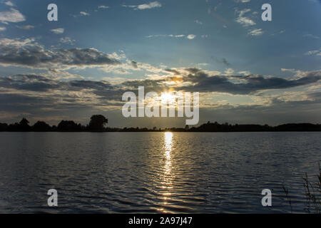 Soleil dans les nuages et de réfléchir la lumière dans l'eau du lac - soirée vue dans Stankow, Lubelskie, Pologne Banque D'Images